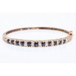 A hallmarked 9ct yellow gold sapphire and diamond hinged bangle, set with eleven graduated round cut