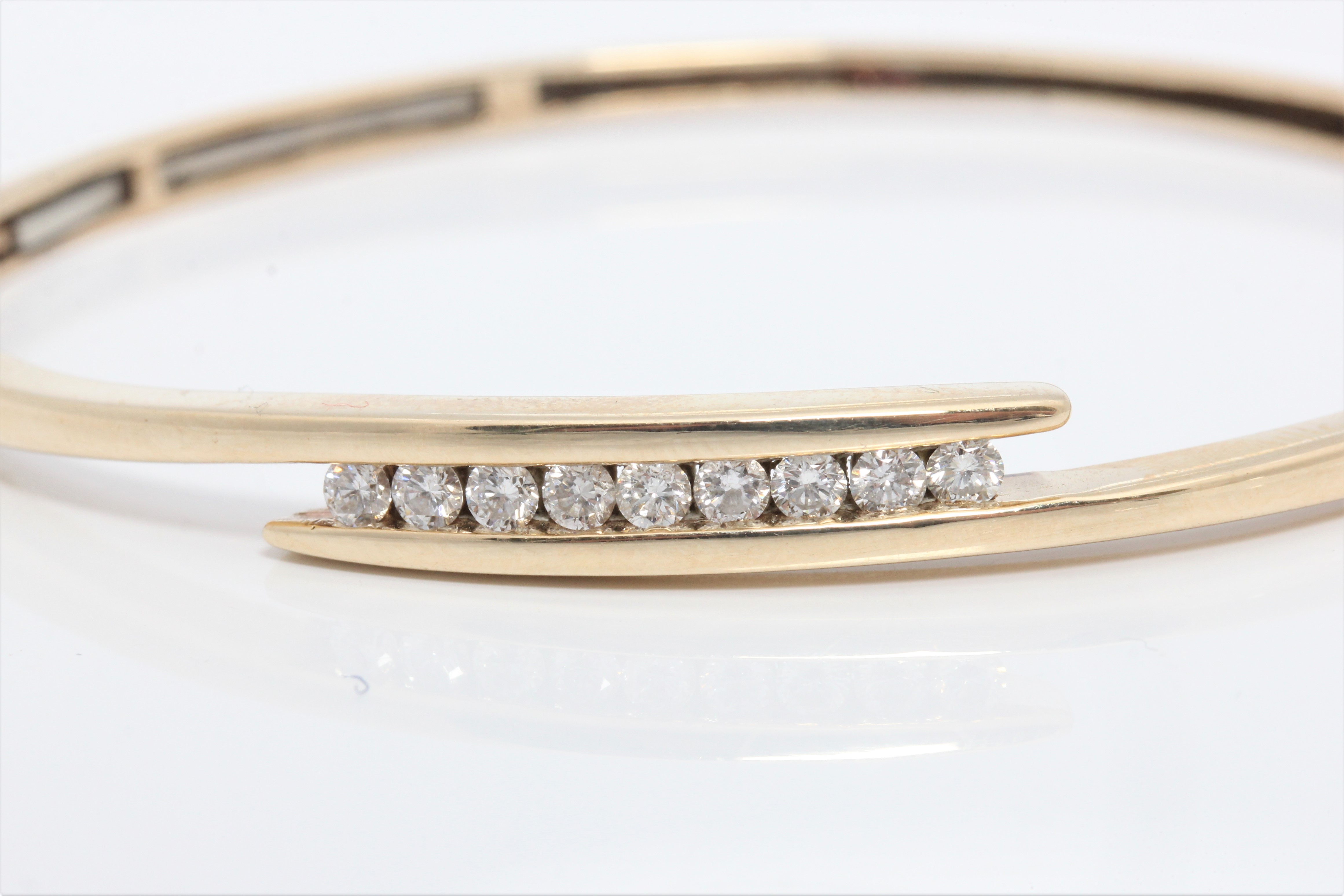 A diamond set bangle, the cross over design set with nine round brilliant cut diamonds, total