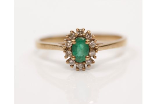 A 9ct yellow gold emerald and diamond cluster ring, set with an oval cut emerald surrounded by a - Image 1 of 4