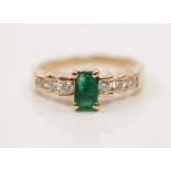 An emerald and diamond ring, set with a central emerald cut emerald measuring approx. 6x4mm, flanked