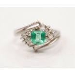 An emerald and diamond ring, set with a central emerald cut emerald, measuring approx. 5x5mm,