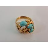 A turquoise ring, set with three oval turquoise cabochons within an open metalwork leaf design,