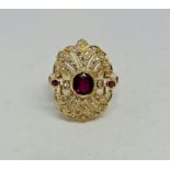A ruby and diamond dress ring, set with a central oval cut ruby, surrounded by open metalwork fan