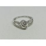 A hallmarked 9ct white gold diamond ring, the open metalwork cross over knot design set with