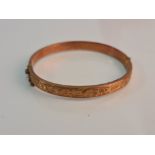 A hallmarked 9ct yellow gold hinged bangle, half engraved with scrolling foliage design, approx.