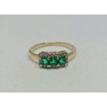 A hallmarked 9ct yellow gold emerald and colourless stone ring, set with three square cut emeralds,