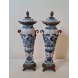 A pair of large decorative vases with blue Chinese village scenes brass handles, rim, finial to