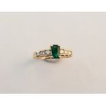 A gold emerald and diamond ring with central rectangular emerald and three diamonds to each