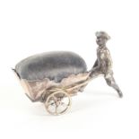 A continental silver pin cushion in the form of a young man in 18th Century costume pushing a