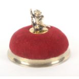 A silver gilt mounted pin cushion by Tiffany and Co., the velvet dome surmounted by a cherub holding