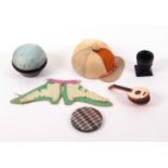 Six pin cushions, comprising a large silk jockey cap example, one segment lacking, 9.5cms, an