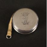A Victorian silver circular tape measure, the complete printed tape in cms and ins., one side