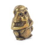 A brass novelty tape measure in the form of a seated monkey, with glass eyes, the reduced printed