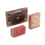 Three leather needle packet cases, comprising a red leather book form example with gilt tooled spine