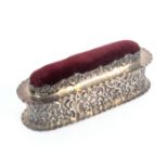 A silver pin cushion box, of rounded end rectangular form decorated with flowers and 'C' scrolls,