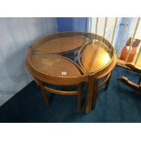 A teak and glass circular coffee table, with three oval small tables