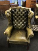 An olive green leather Chesterfield wing armchair