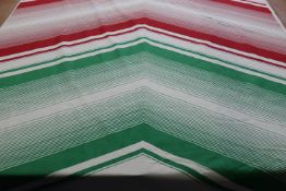 A roll of screen painted cotton fabric, the cream ground having a large red and green arrow