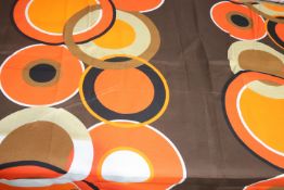 A piece of fabric, the brown ground with overlapping circles in orange, white, brown and black,