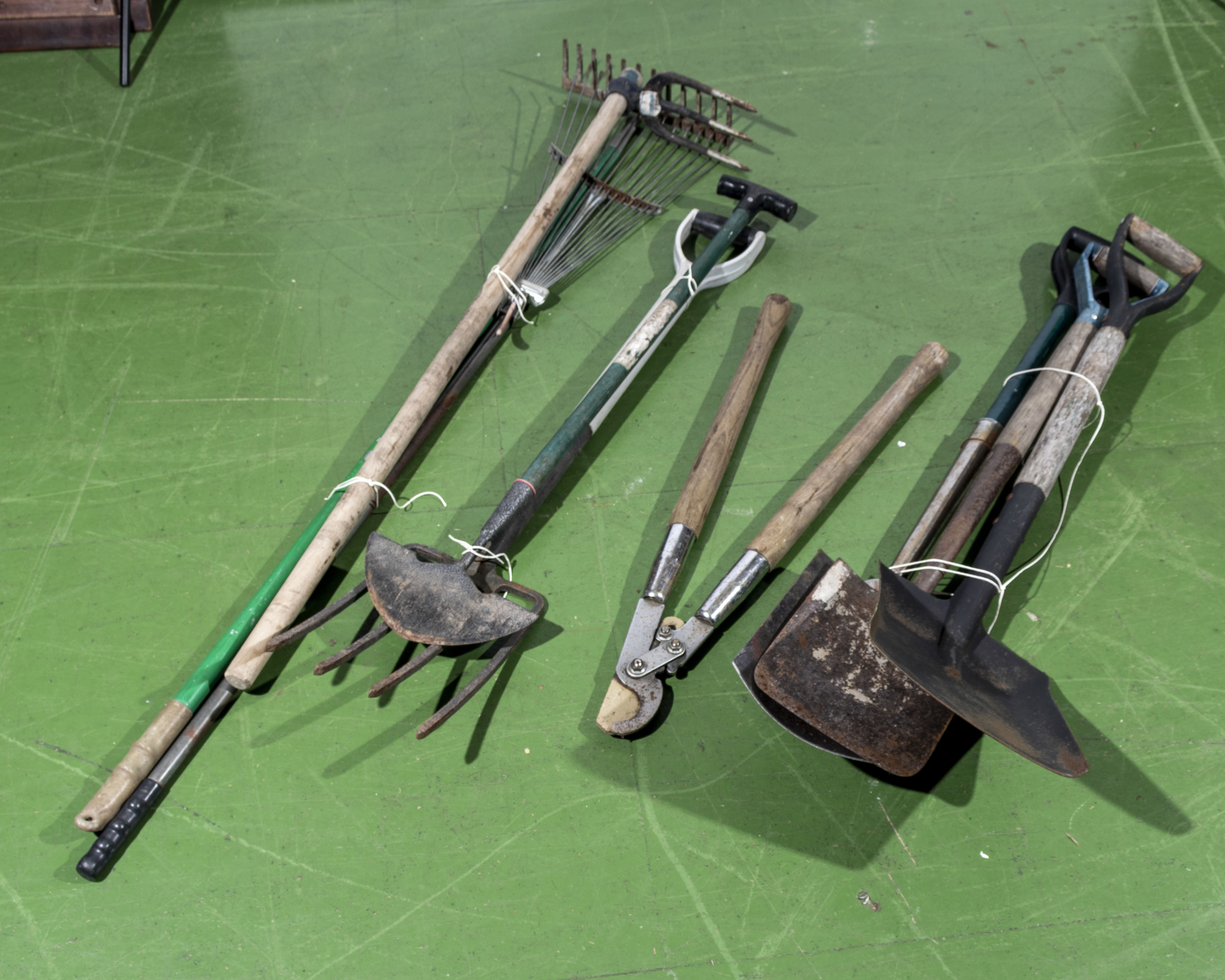 A bundle of garden tools, three spades, loppers, hoe, rakes and forks