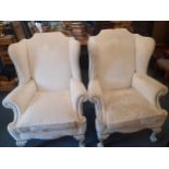 A pair of cream upholstered wing back armchairs with stud detail to arms and trim having white