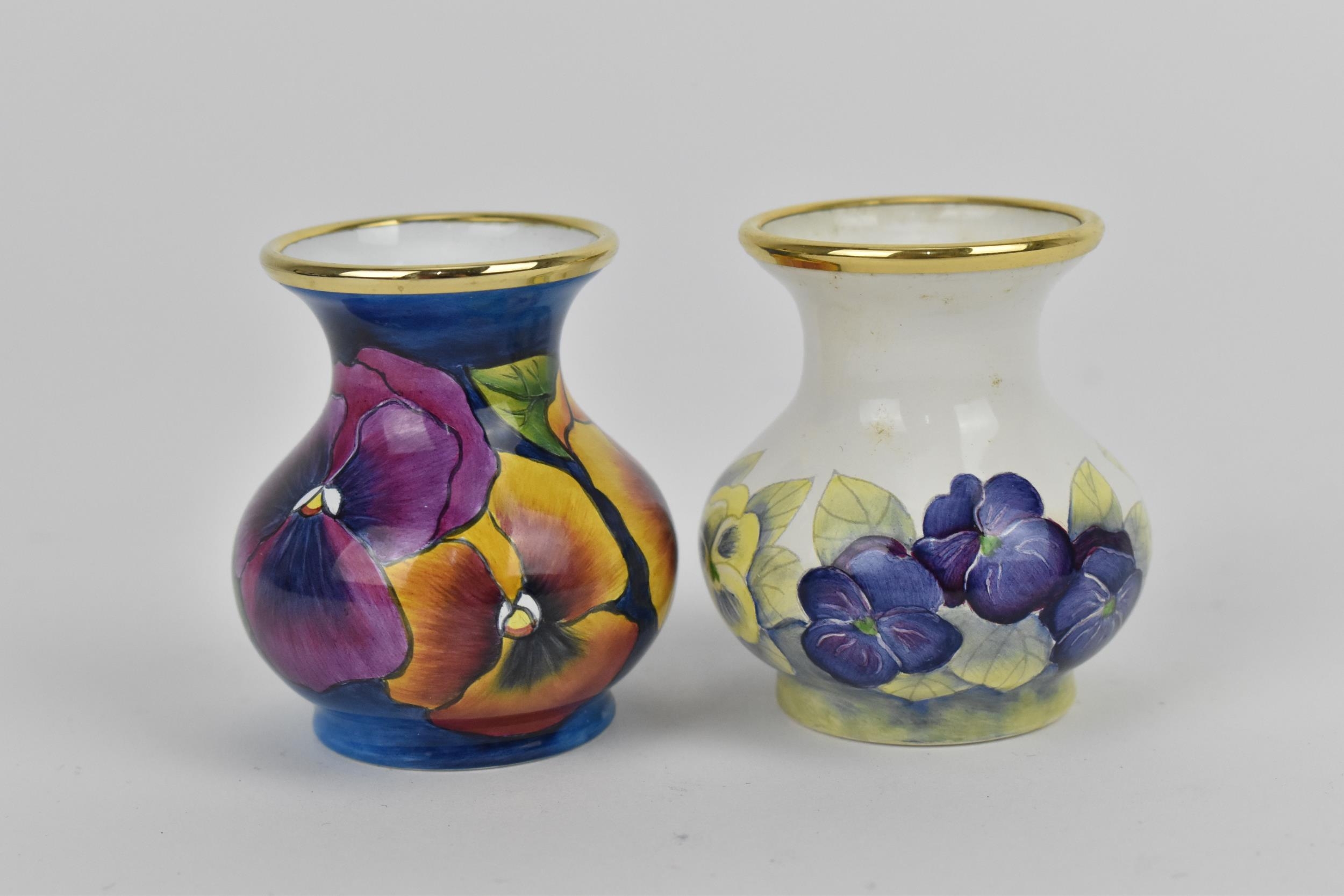 Two Moorcroft Enamels Ltd miniature vases, both of baluster form with painted pansies, the blue