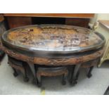 An oriental heavily carved oval coffee table with six slide cut matching tables, 52cm h x 130cm w