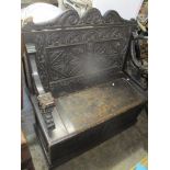 An early 20th century oak carved two seater settle/bench having shell and scroll carved pediment and