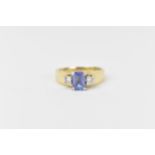 A 14ct yellow gold, tanzanite and diamond ring, the central emerald cut cornflower tanzanite flanked