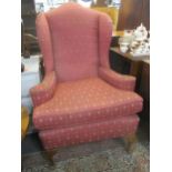 An early 20th century upholstered wing back armchair with loose seat cushion, on short cabriole