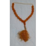 A Vintage amber necklace comprising eighteen chunky oval beads on an embroidered and tasselled