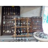 Collectors teaspoons in four wall shelves to include a Rolex teaspoon and silver plated examples and