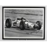 A signed reprinted photograph of Dan Gurney in a racing car, within a glazed frame, 30 x 40 cm