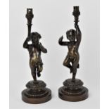 A pair of late 19th century patinated bronze figural lamps, each modelled as a putto holding the