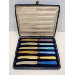 A cased set of six silver rimmed butter knifes with enamelled handles and gilded blades Location: