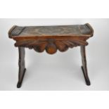 A 19th century continental oak stool, the carved top with upturned ends and a shaped apron, on