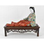 A Japanese kutani porcelain model of a geisha, early 20th century, raised on a wooden stand, the