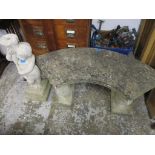 A weathered stone bench, the curved half-moon shaped top with moulded edge, resting on two pedestals