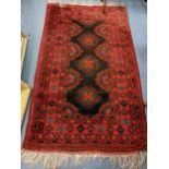 A Middle Eastern hand woven red ground rug having repeating motifs and tasselled ends, 183cm x 108cm