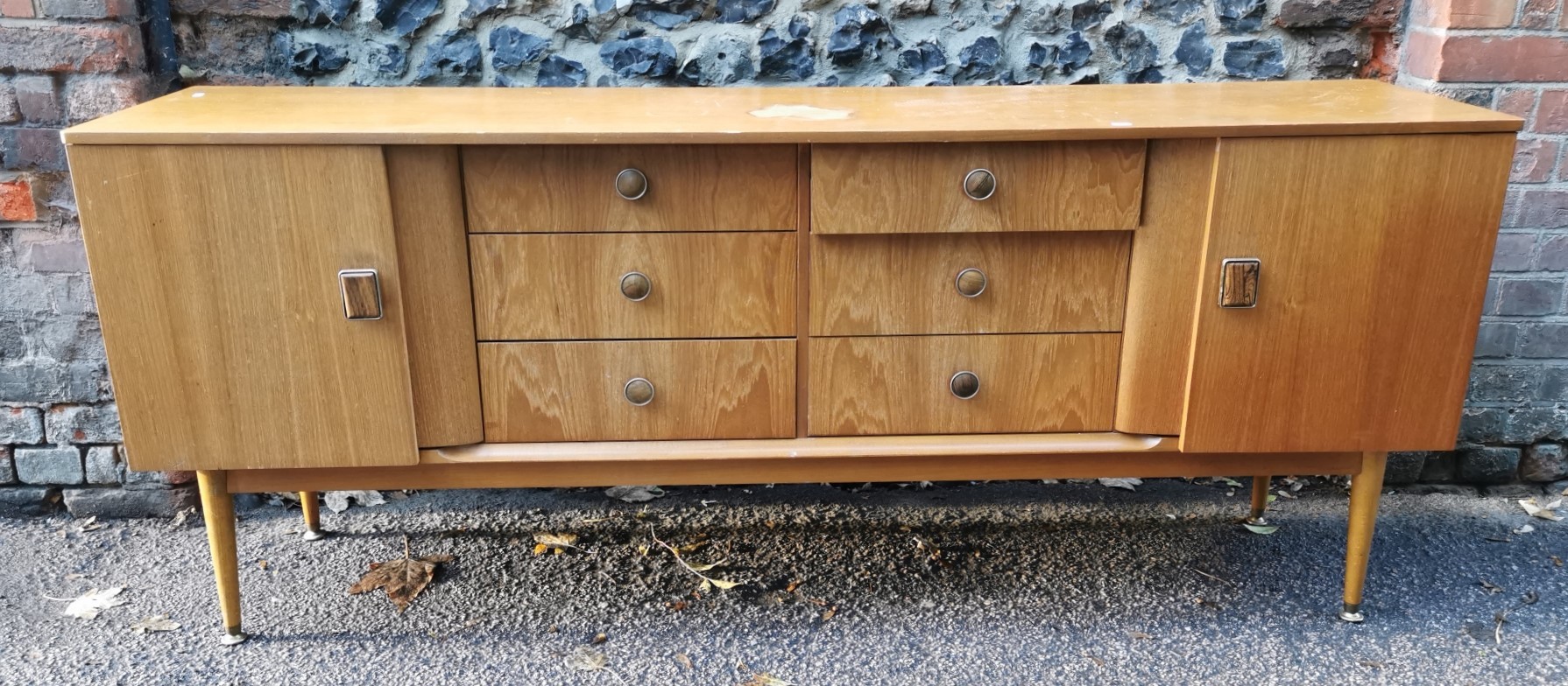A 1970s design light teak sideboard, with six drawers to the centre flanked by a cupboard door