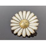A silver gilt and enamel brooch fashioned as a daisy, with a textured centre and white leaves,