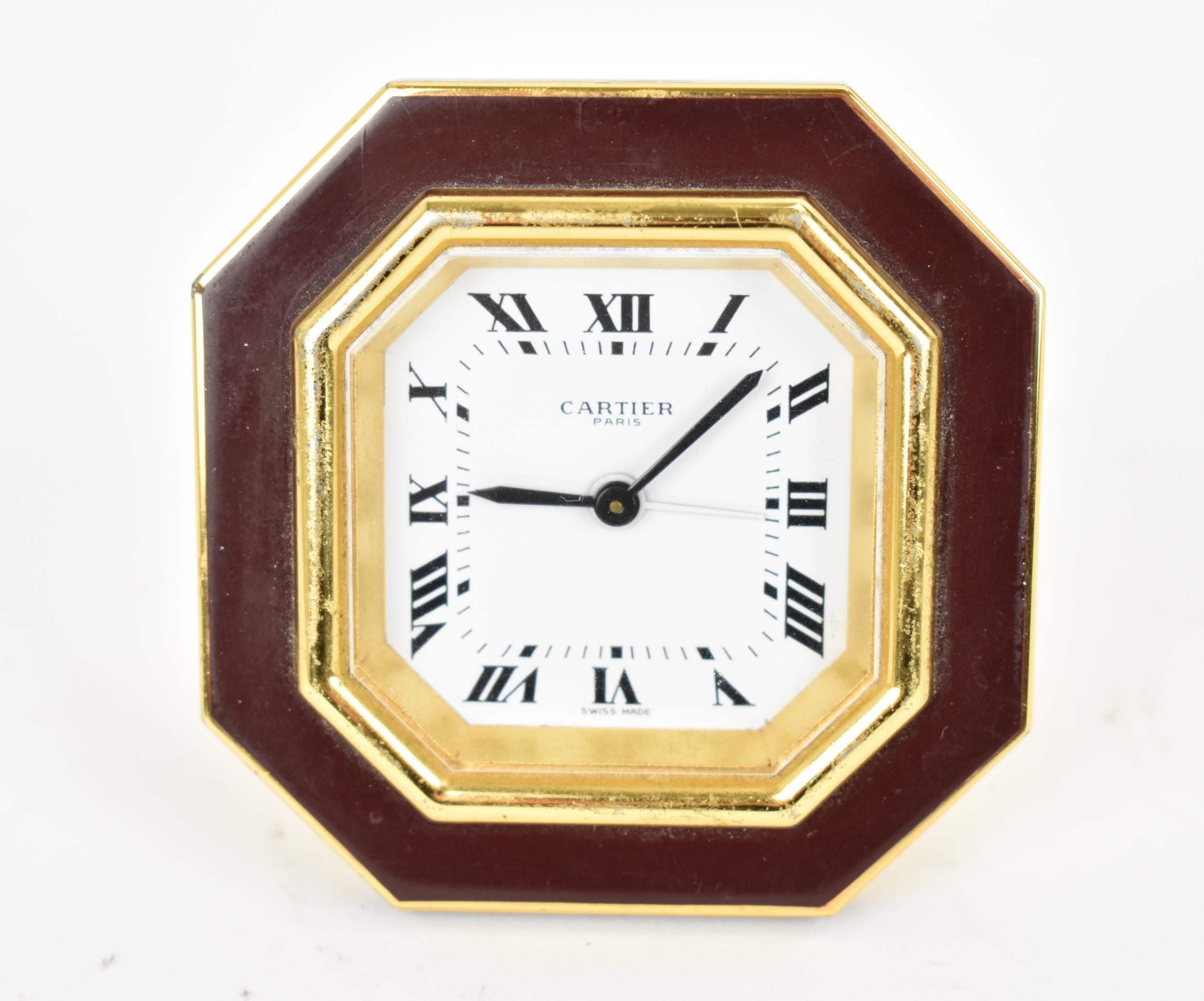 A Cartier manual wind, gilt brass and burgundy enamel travel clock having a white enamel dial with