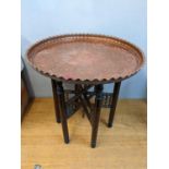 An Egyptian table with an embossed copper tray, on a folding stand, 63cm h, 60cm dia