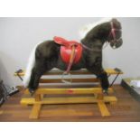 A pine framed rocking horse upholstered in brown with a white mane and tail, red leather saddle with