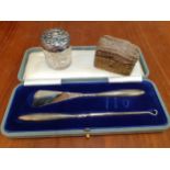 A white metal topped and glass dressing table pot, a brass and brown velvet pin cushion and cased