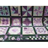 A handmade quilt in purples and greens with a floral and checkerboard border, worked by Mary