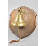 A Brass Bell Mounted on Oak Shield Wall Hanging Plinth, 34cms High