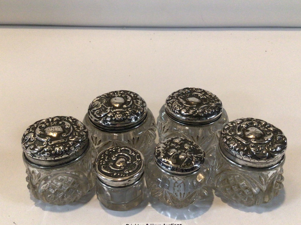 SIX HALLMARKED SILVER EMBOSSED TOP GLASS TOILET BOTTLES