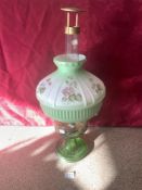 A LATE VICTORIAN GREEN GLASS OIL LAMP WITH BRASS FIXTURES AND WITH A FLORAL DECORATED OPAQUE GLASS