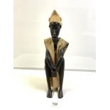 A CARVED WOODEN TRIBAL FIGURE OF A SEATED MAN, WITH A CANVAS ROBE 48 CM